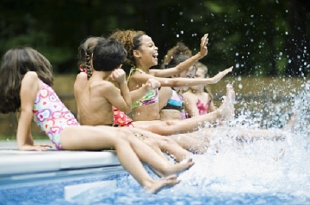 Kids Kicking Up Water Seated on the Edge of a Pool